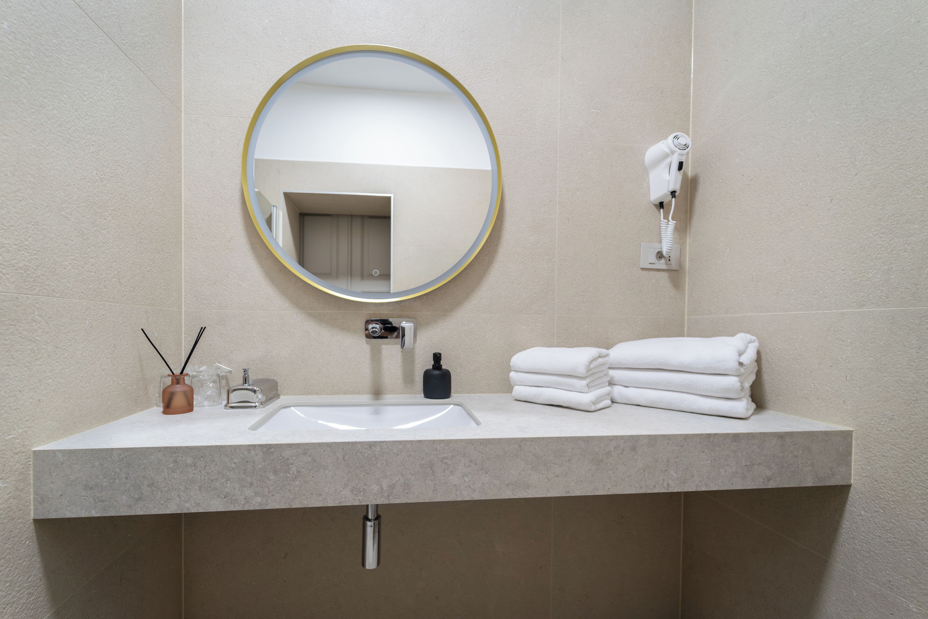 A bathroom with a round mirror, a sink, a towel rack, and a hairdryer.