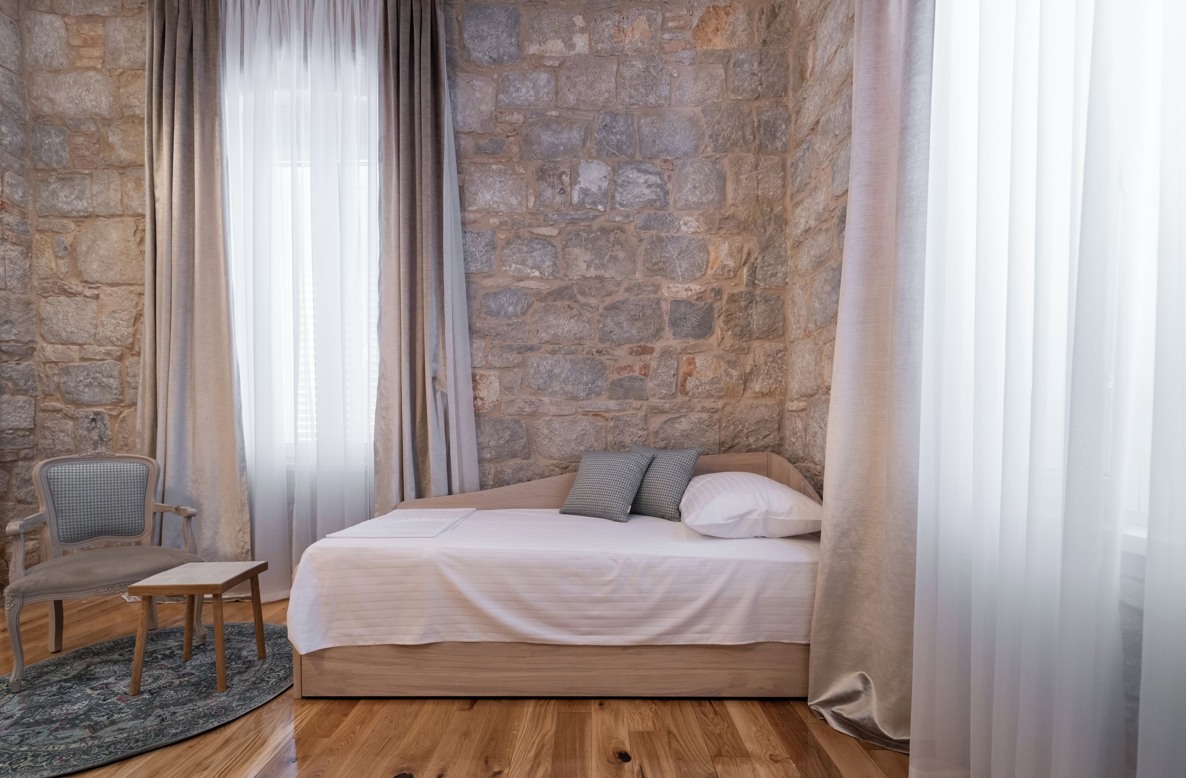 Ein Schlafzimmer mit Steinwand, einem Bett mit Kissen, einem Sessel und einem kleinen Tisch.