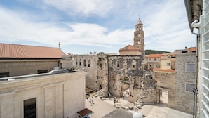 Una plaza histórica con edificios de piedra, una torre de campanas y un pequeño quiosco.