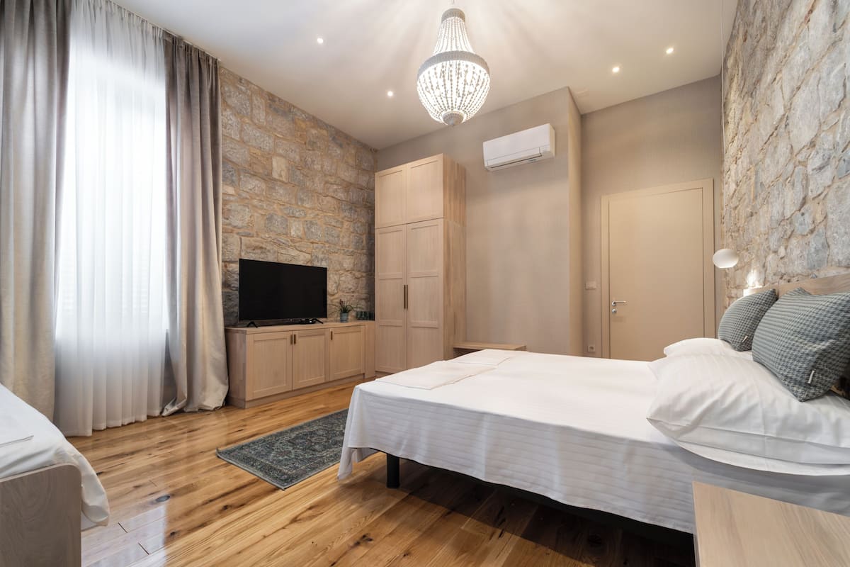 Un dormitorio con pared de piedra, muebles de madera, una araña y un televisor de pantalla plana.
