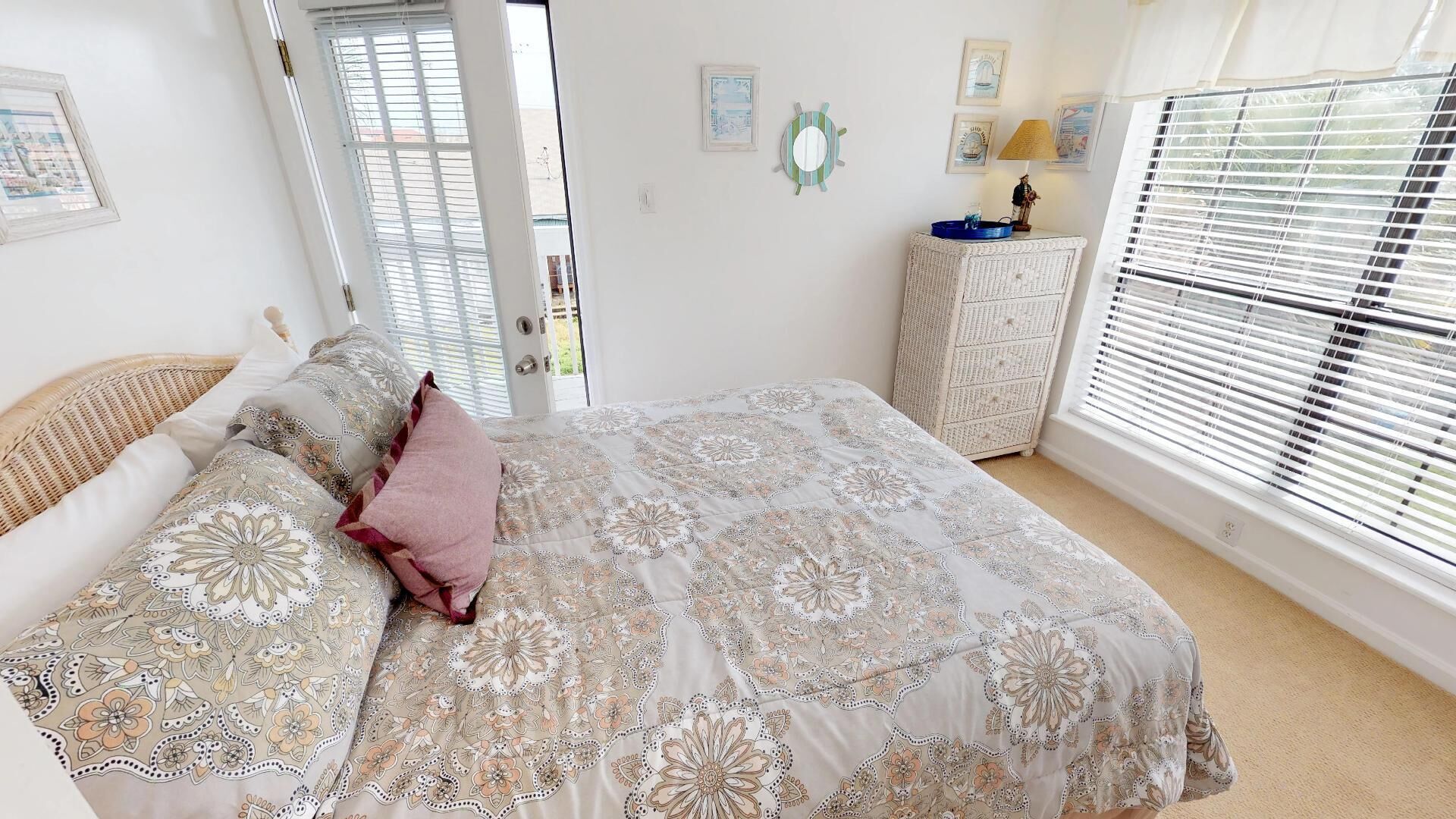 A bedroom with a large bed, a wicker chair, a dresser, and a window with blinds.