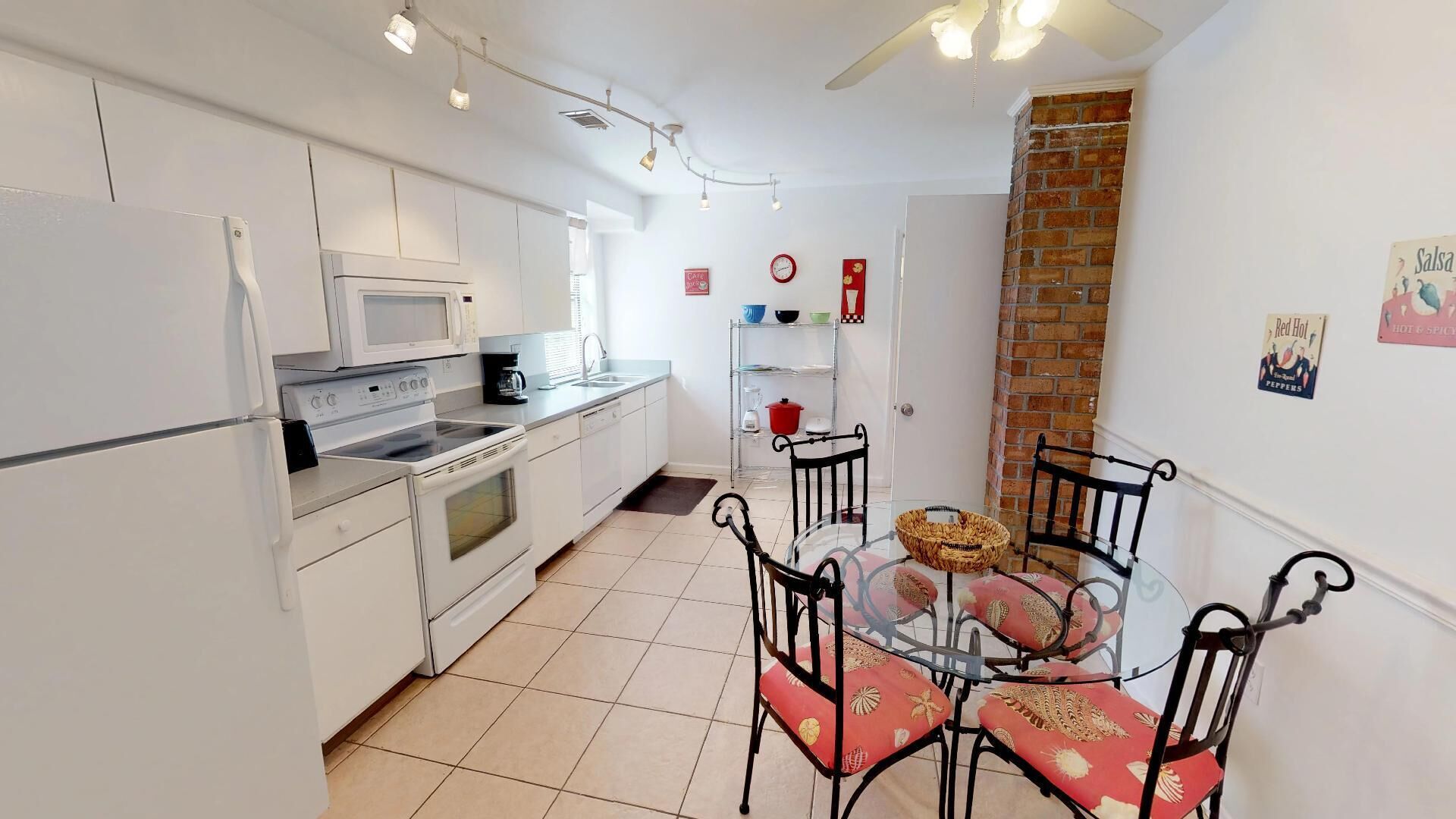Une cuisine compacte avec des meubles blancs, un four à micro-ondes, une cuisinière et un coin repas comprenant une table en verre et des chaises en métal.