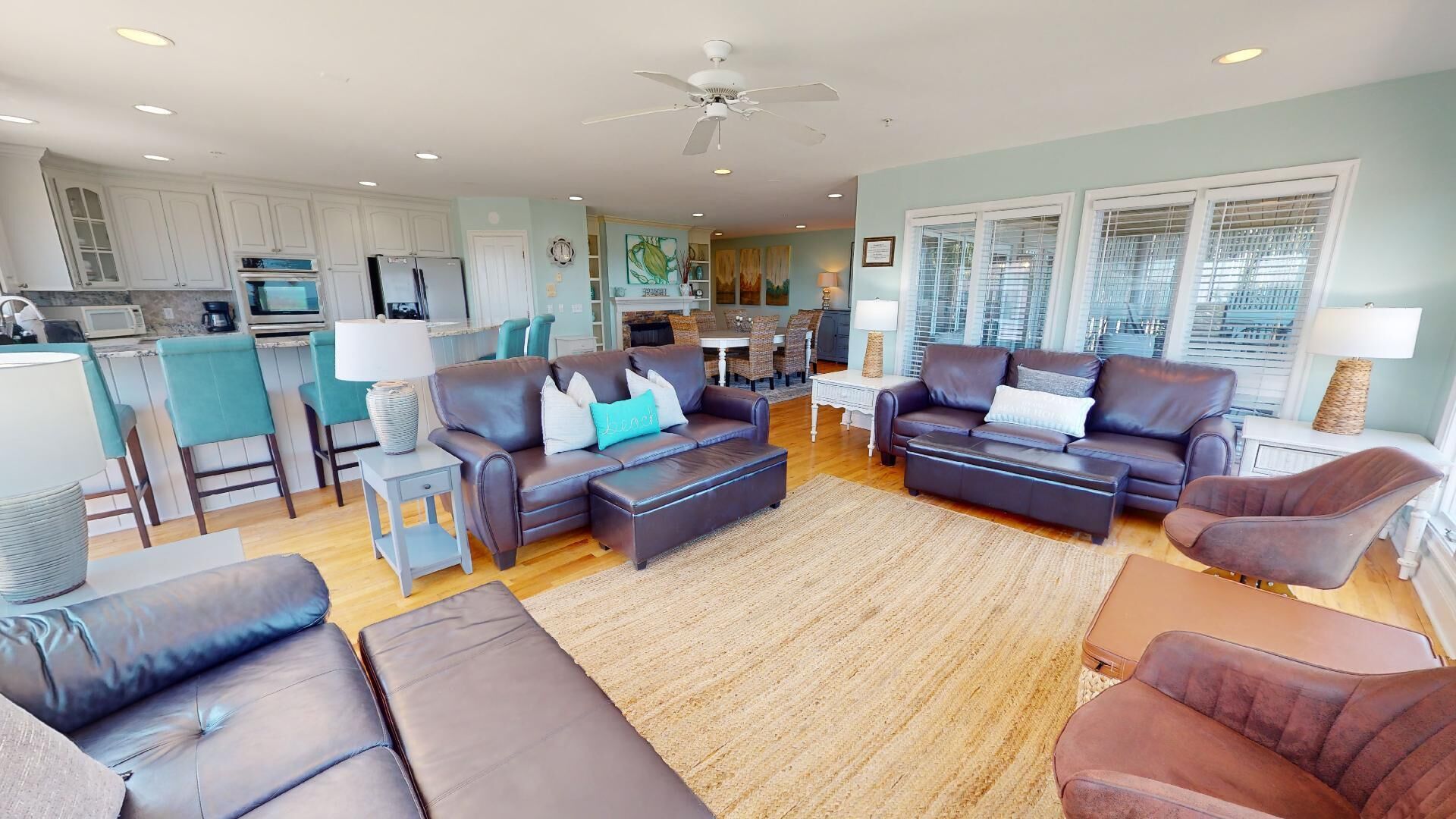 A spacious living area with leather sofas, a coffee table, and a dining table. There is a kitchen with white cabinets and a dining area with chairs.