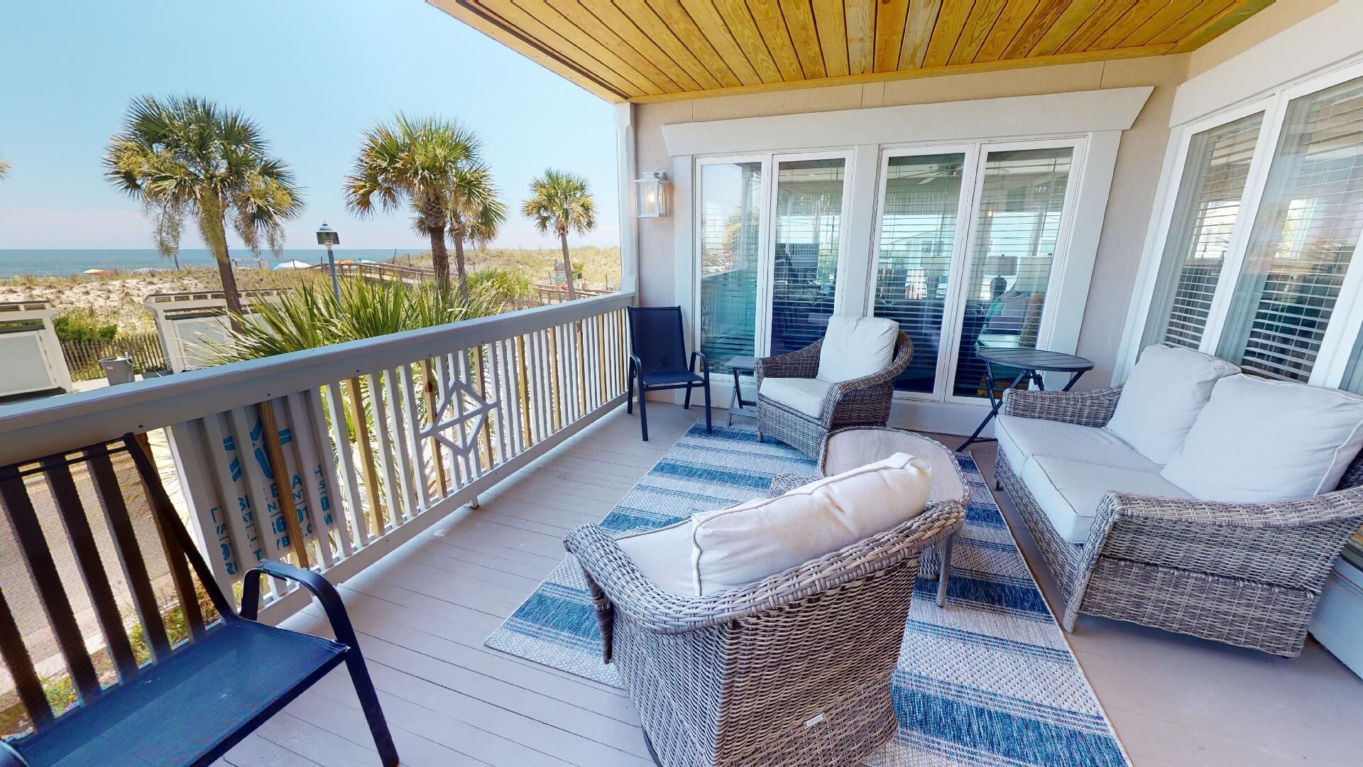 A covered outdoor area with wicker furniture, a view of the beach, and a wooden ceiling.