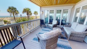A covered outdoor area with wicker furniture, a view of the beach, and a wooden ceiling.