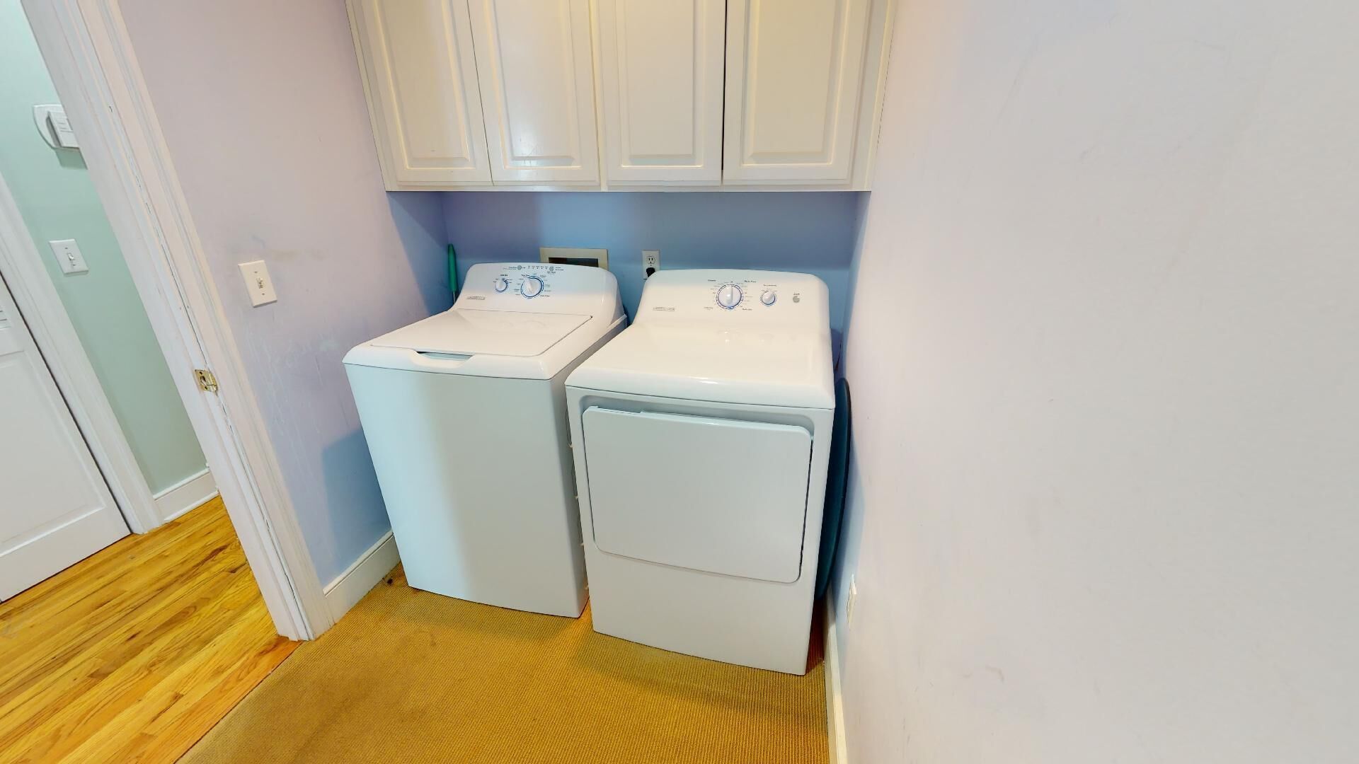 A laundry room with two white front-loading washing machines and a door to the left.
