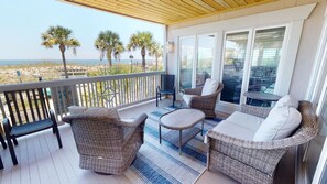A covered balcony with wicker furniture, a view of the beach, and a wooden ceiling.