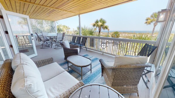 A covered outdoor area with wicker furniture, a table, and a view of the beach.