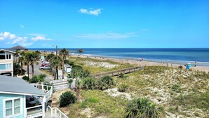 A beach view with a wooden boardwalk, beach umbrellas, and a pier in the background. - 1801-B Strand Avenue by Tybee Vacation Rentals (Tybee Island)