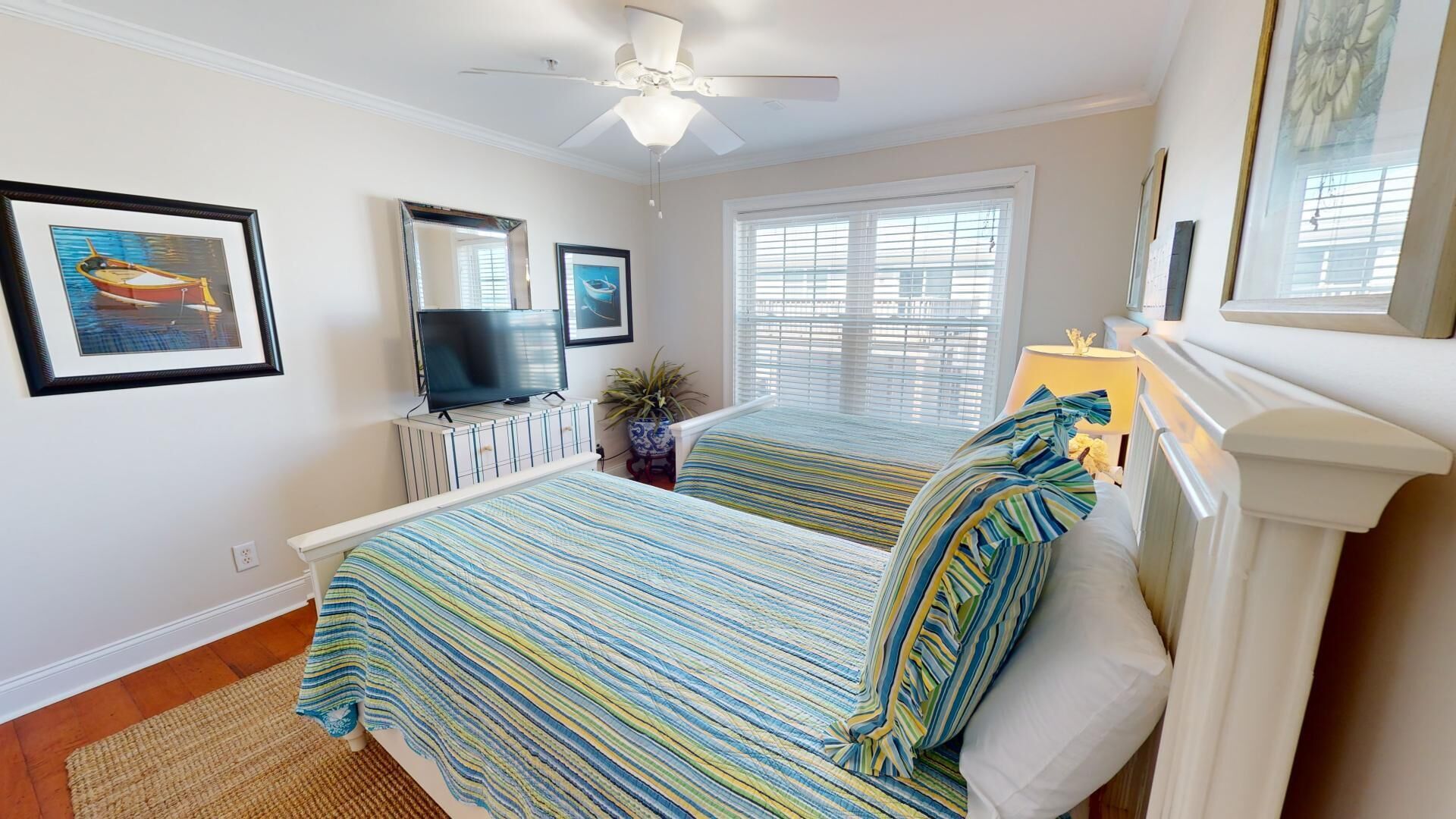 A bedroom with two beds, a ceiling fan, a TV, and framed pictures on the wall.