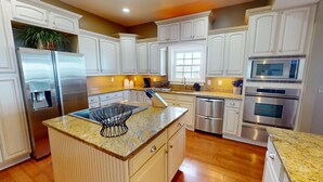 A modern kitchen with white cabinetry, stainless steel appliances, granite countertops, and a central island with a sink and a black wire basket. - 1801-B Strand Avenue by Tybee Vacation Rentals (Tybee Island)