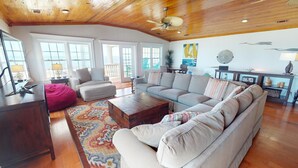 A spacious living room with a wooden ceiling, large windows, and a variety of seating including a sofa, chairs, and a bean bag. - 1801-B Strand Avenue by Tybee Vacation Rentals (Tybee Island)