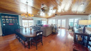 A spacious living area with a wooden ceiling, a dining table with chairs, and a kitchen area with a cabinet and decorative plates. - 1801-B Strand Avenue by Tybee Vacation Rentals (Tybee Island)