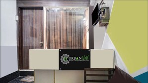 A reception desk with a sign for URBAN Nest, a room layout with a bed and a chair, and a sliding door in the background. - Urban Nest Rooms & Rooftop Restaurant (Noida)