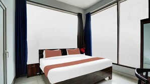 A modern hotel room with a large bed, dark wood headboard, and a view through floor-to-ceiling windows. - Urban Nest Rooms & Rooftop Restaurant (Noida)