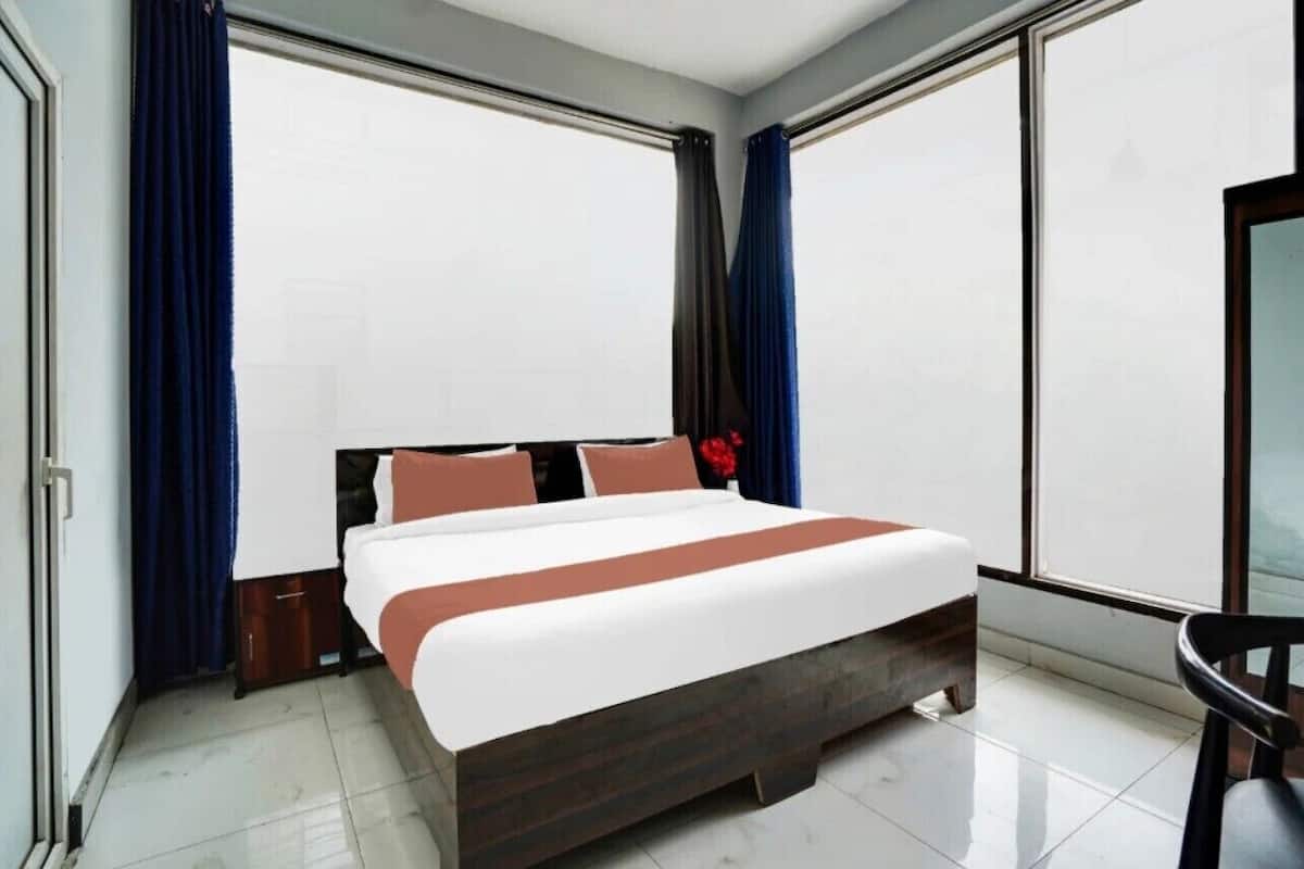 A modern hotel room with a large bed, dark wood headboard, and a view through floor-to-ceiling windows.