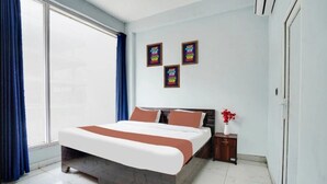 A modern bedroom with a large bed, a nightstand, and a vase of flowers. There are three framed motivational posters on the wall. - Urban Nest Rooms & Rooftop Restaurant (Noida)