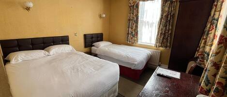 A hotel room with two beds, a wooden desk with a coffee maker, and a window with floral curtains.