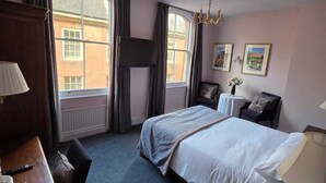 Habitación de hotel con una cama grande, un escritorio con lámpara, una silla y vista a un edificio desde la ventana.