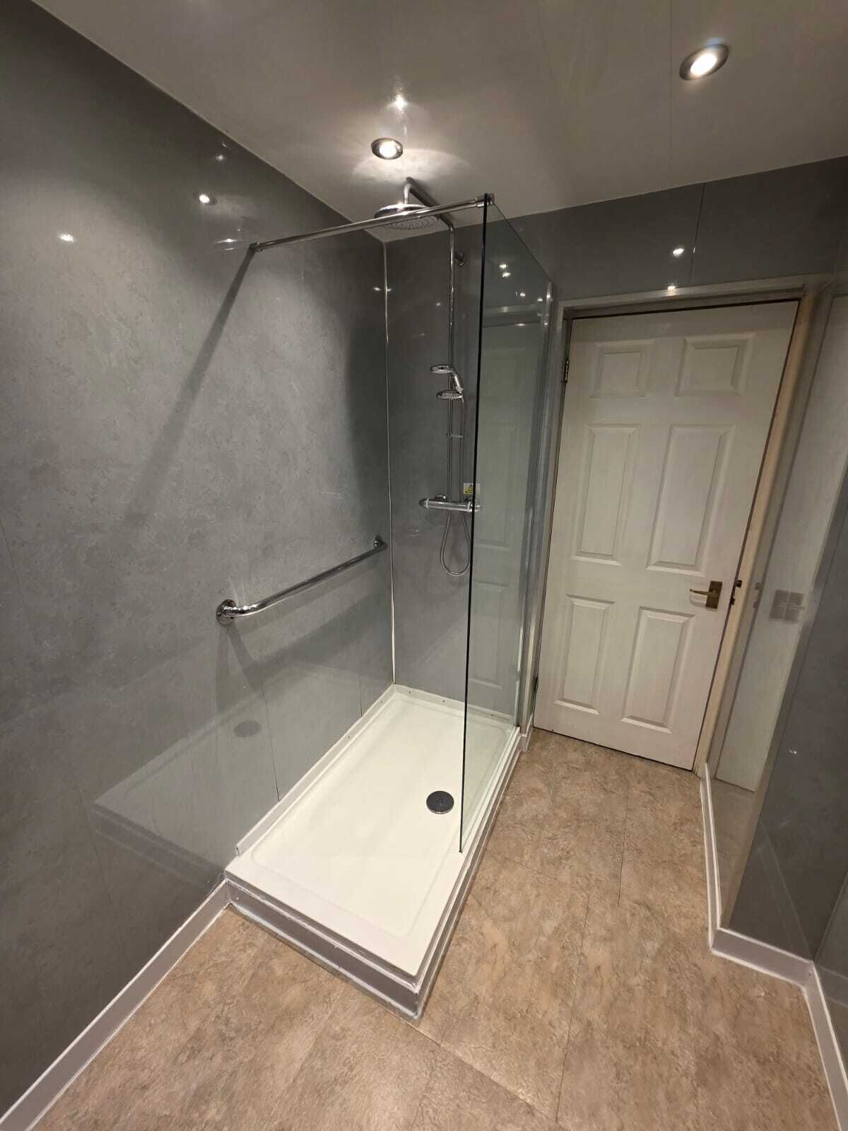 A modern bathroom with a glass-enclosed shower, a white door, and beige tiles.