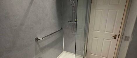 A modern bathroom with a glass-enclosed shower, a white door, and beige tiles.
