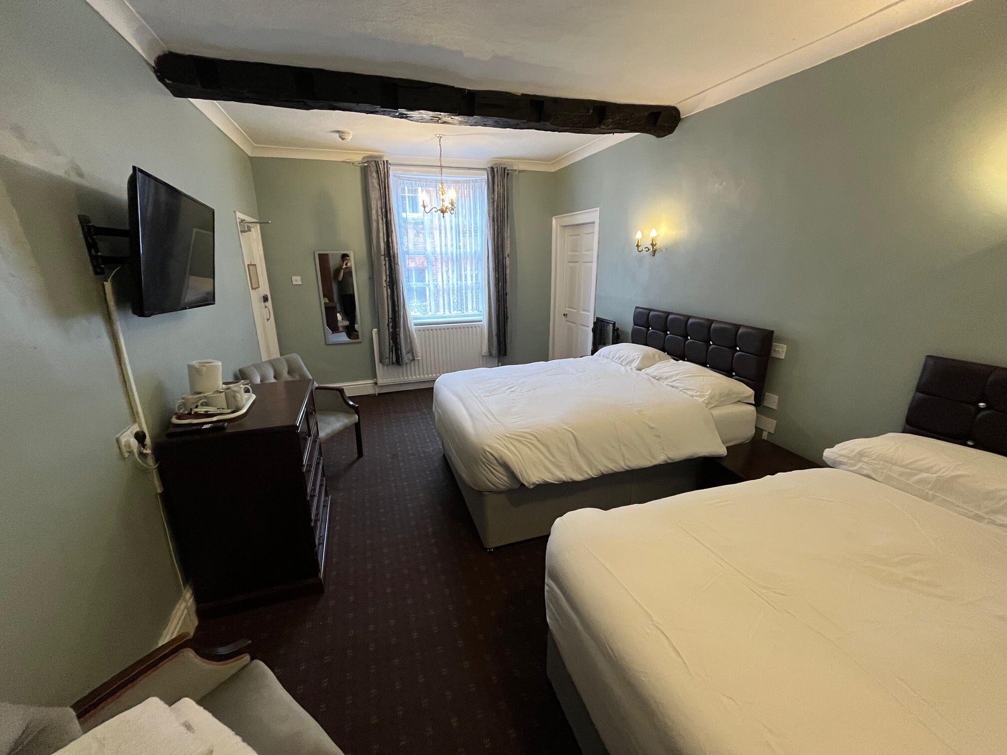 A hotel room with two beds, a desk, a chair, a TV, and a window with curtains.