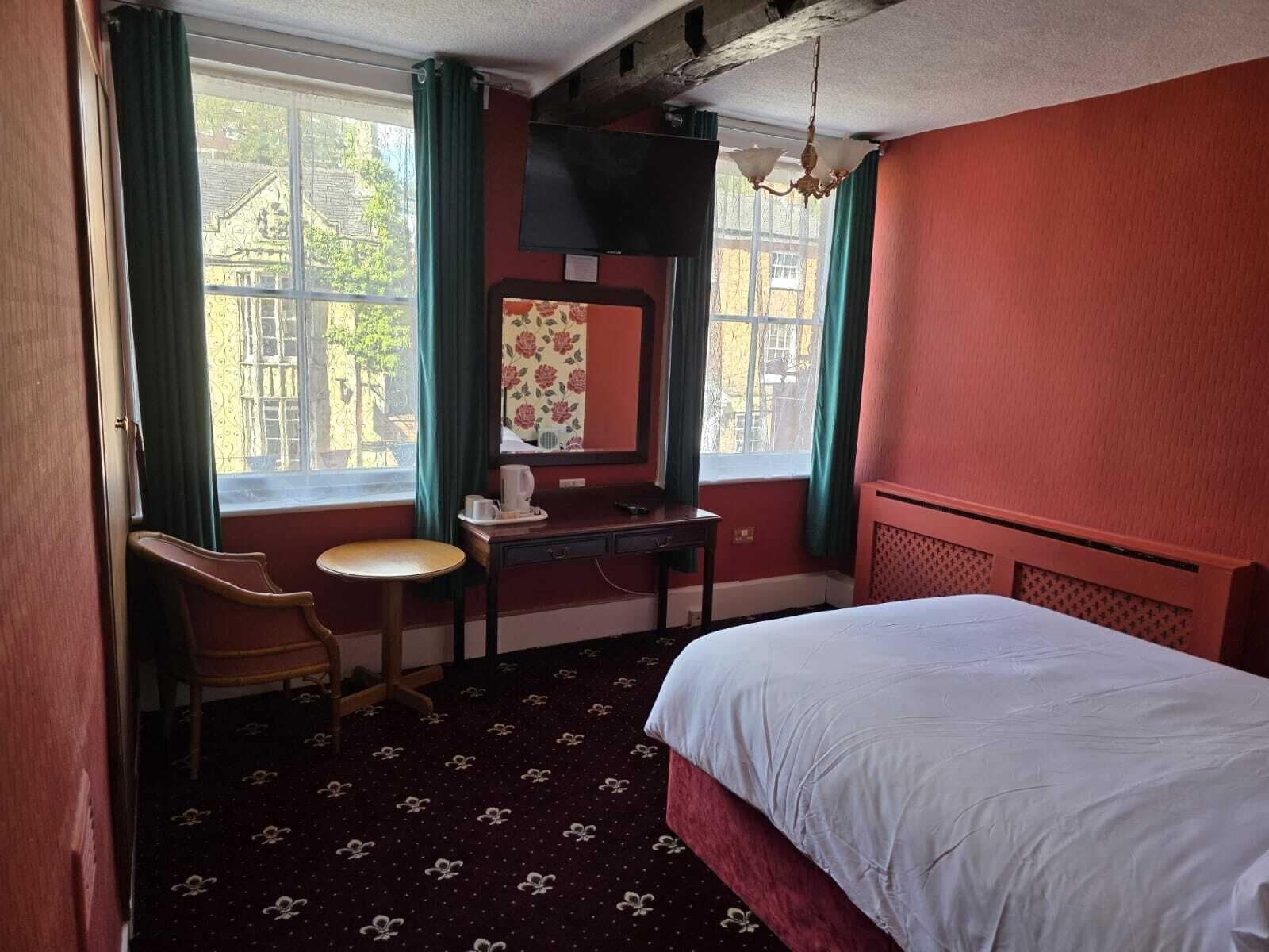 A hotel room with a bed, a desk, a chair, a television, and a window with curtains.