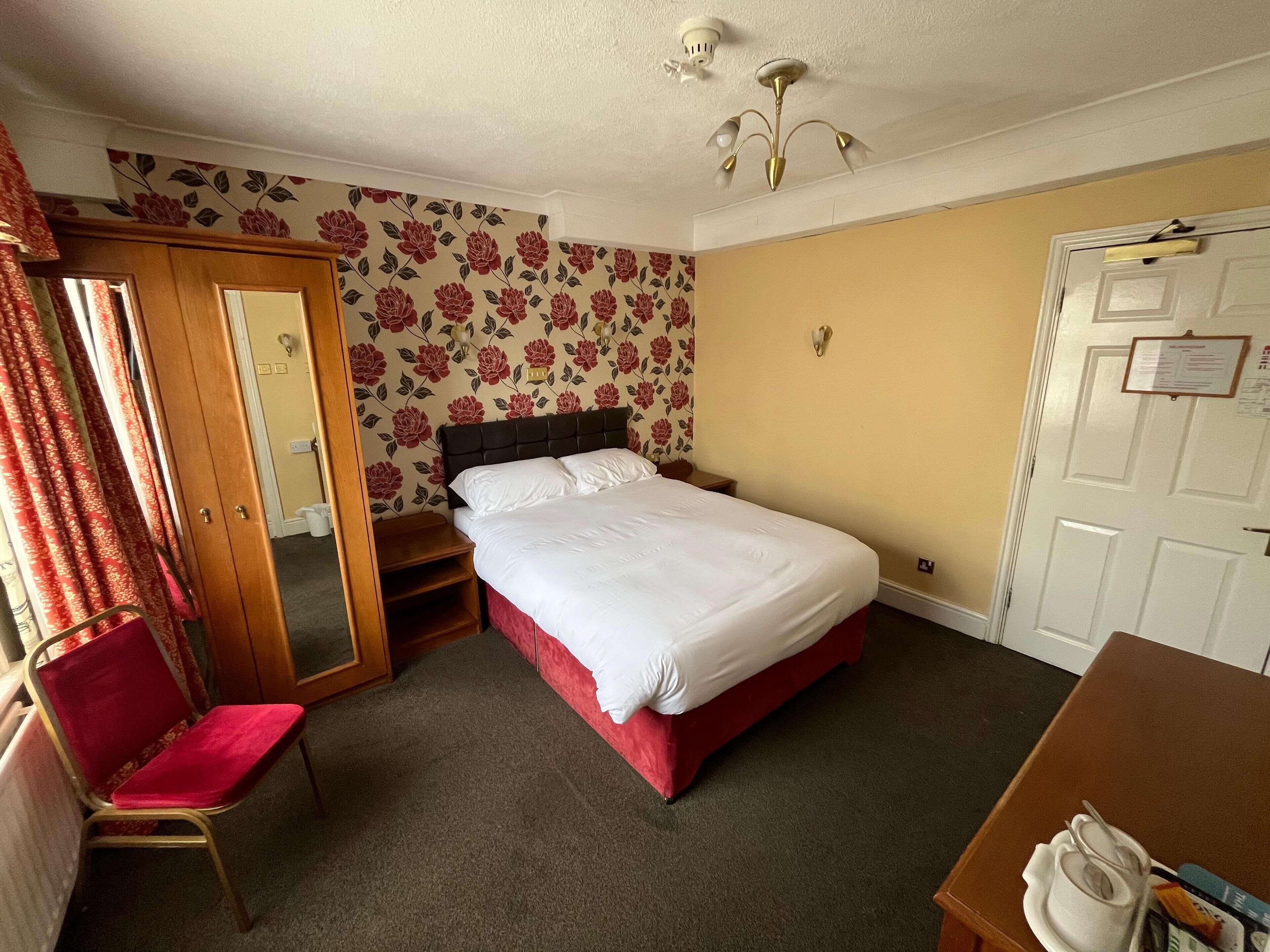 A hotel room with a bed, a chair, a desk, and a door.