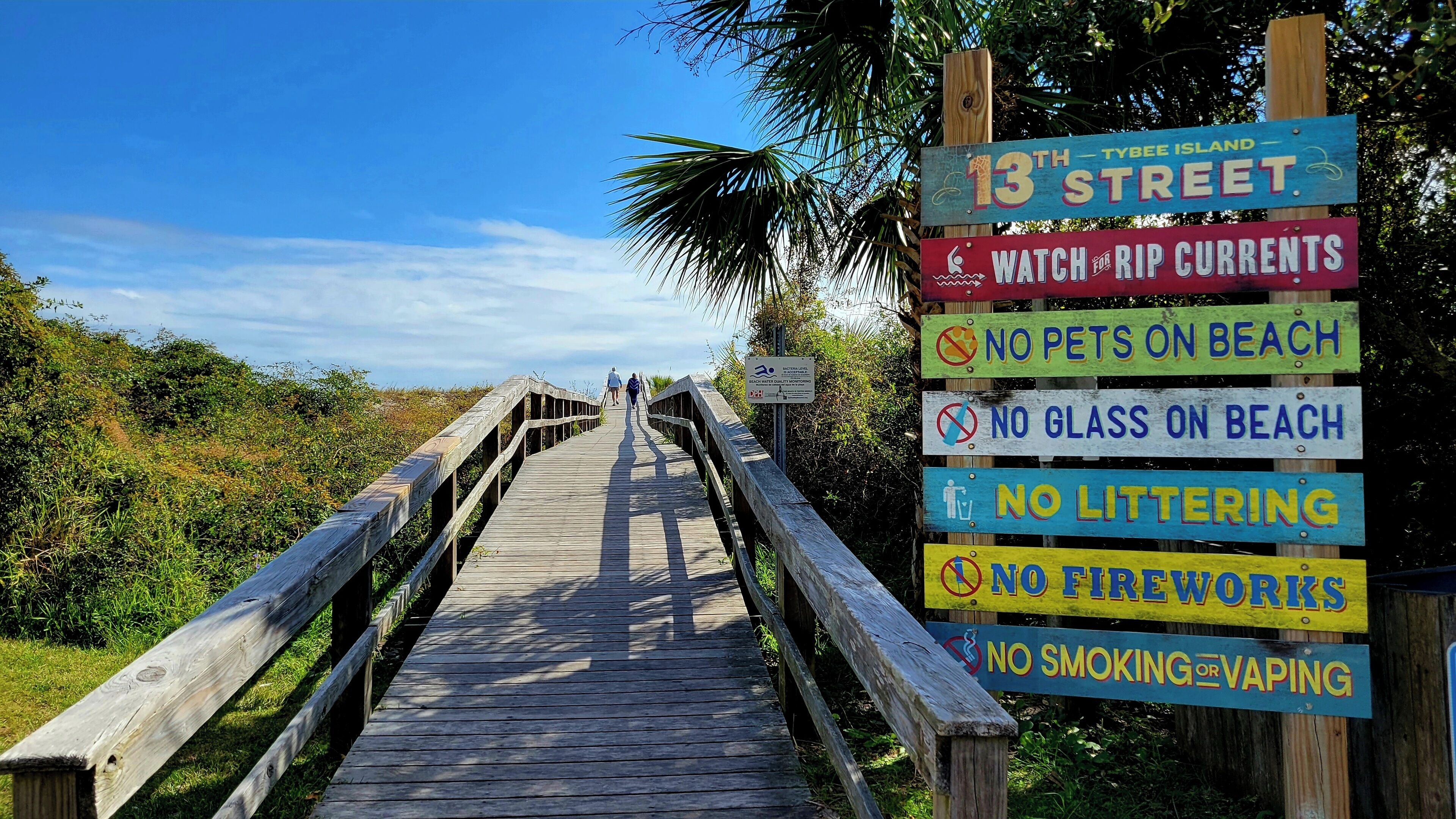 Uma passarela de madeira que leva à Ilha Tybee, com placas indicando proibição de animais de estimação, vidro, lixo, fogos de artifício, fumar ou vapores eletrônicos.