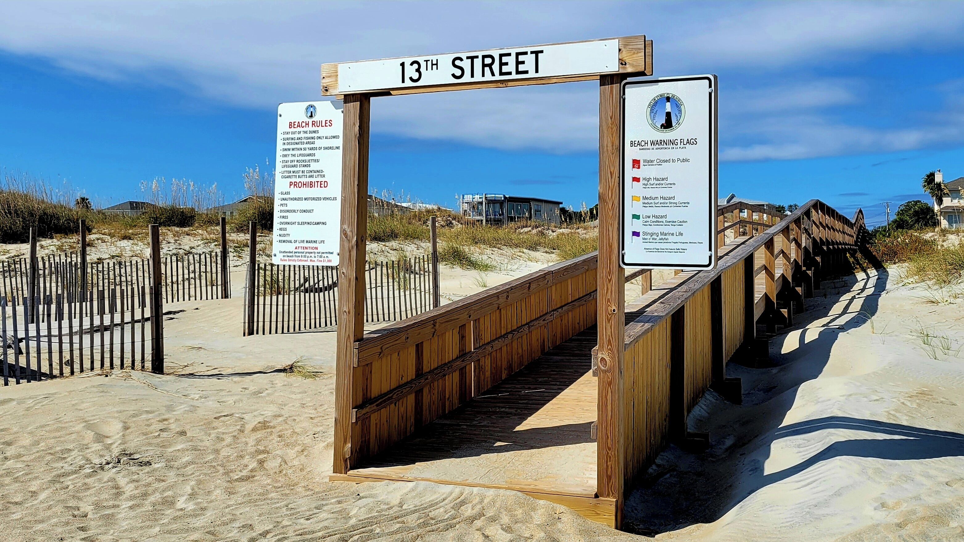A wooden boardwalk leading to a beach with signs indicating beach rules and warning flags.