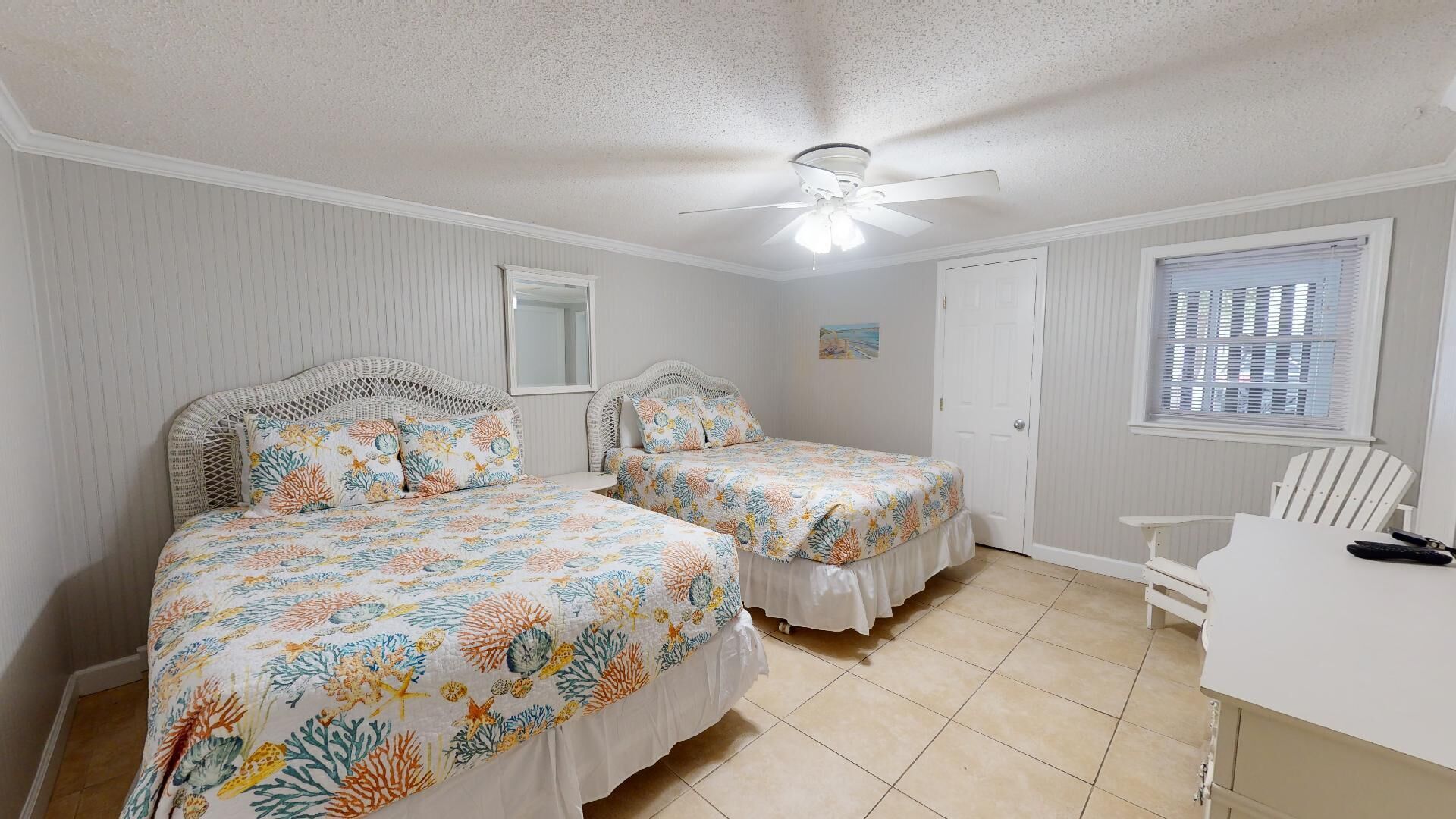 A bedroom with two beds, a ceiling fan, a window with blinds, and a white chair.