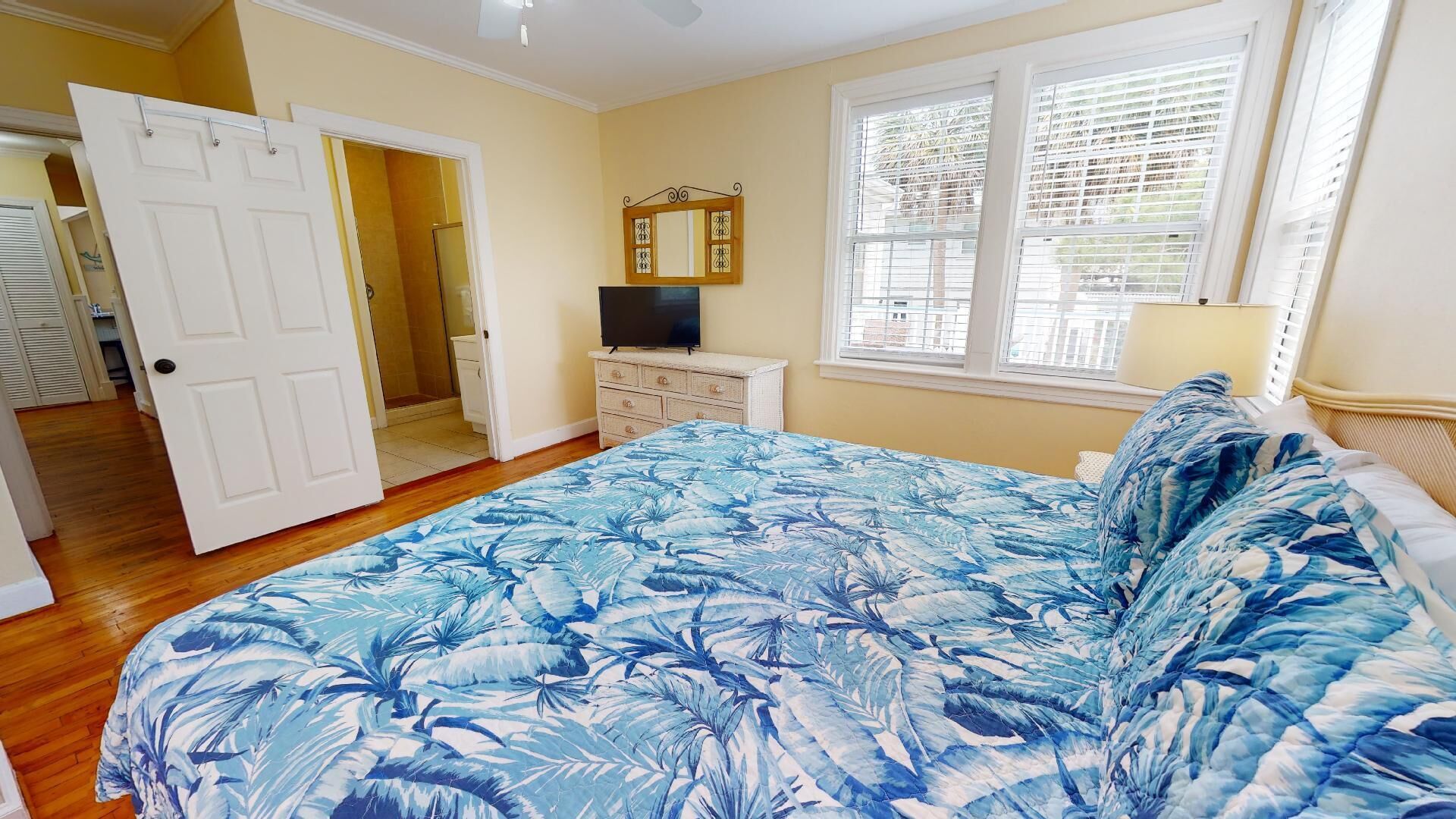 A bedroom with a bed, a television, a dresser, and a window with blinds.