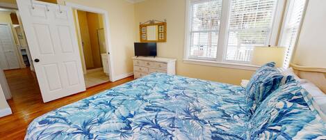 A bedroom with a bed, a television, a dresser, and a window with blinds.