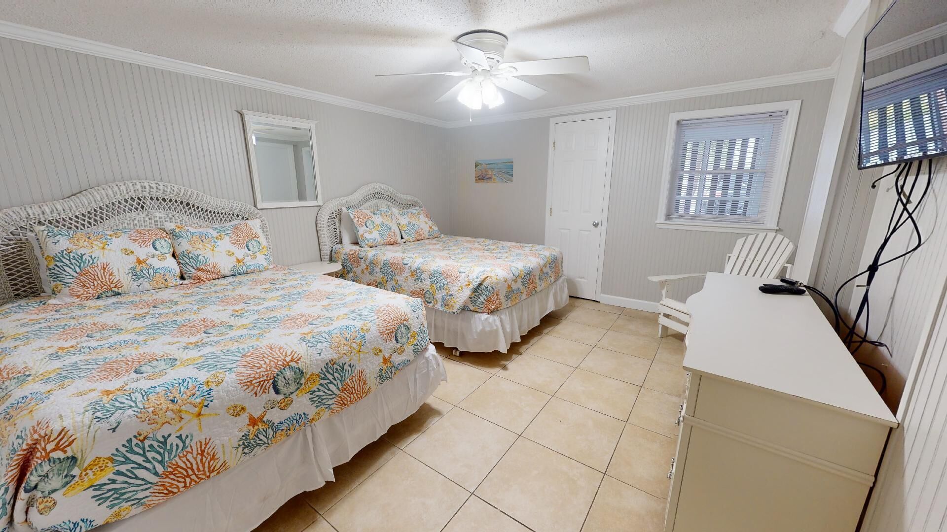A bedroom with two beds, a desk, a chair, a ceiling fan, a window with blinds, and a door.