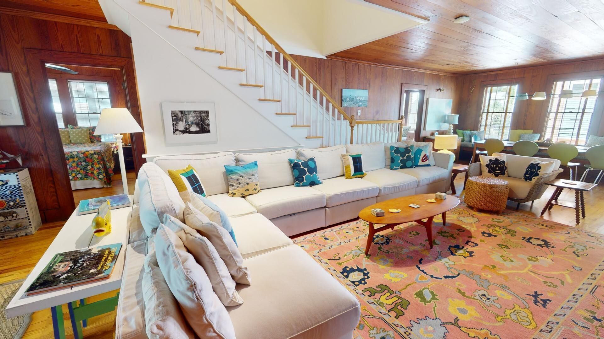 A spacious living room with a white sofa, colorful cushions, a coffee table, and a staircase leading to another level.