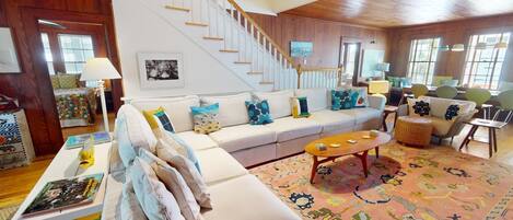 A spacious living room with a white sofa, colorful cushions, a coffee table, and a staircase leading to another level.