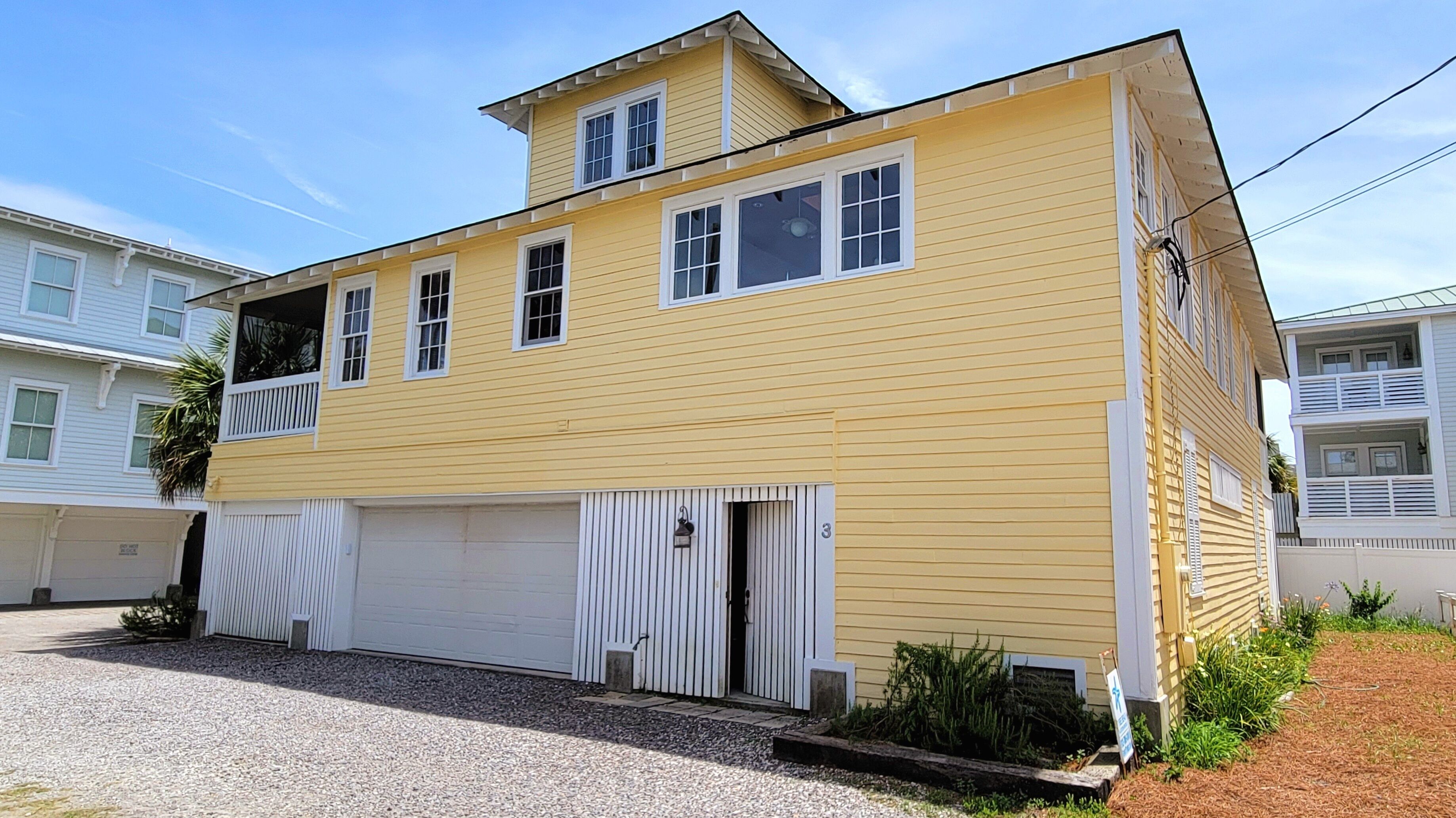 A two-story yellow building with a white garage door, a small balcony, and a number '3' on the side.