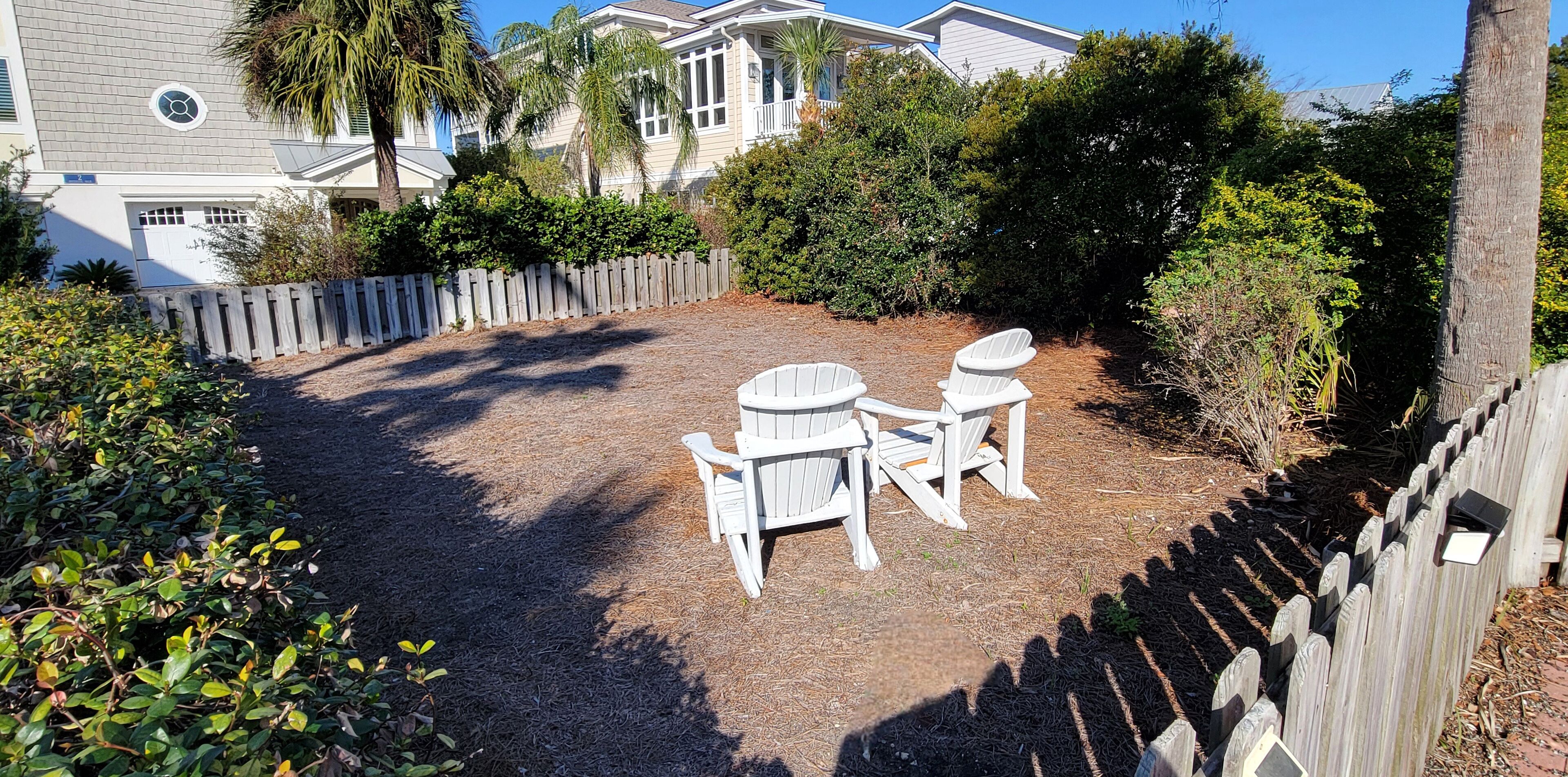 A backyard with a wooden fence, two Adirondack chairs, and a patio area.