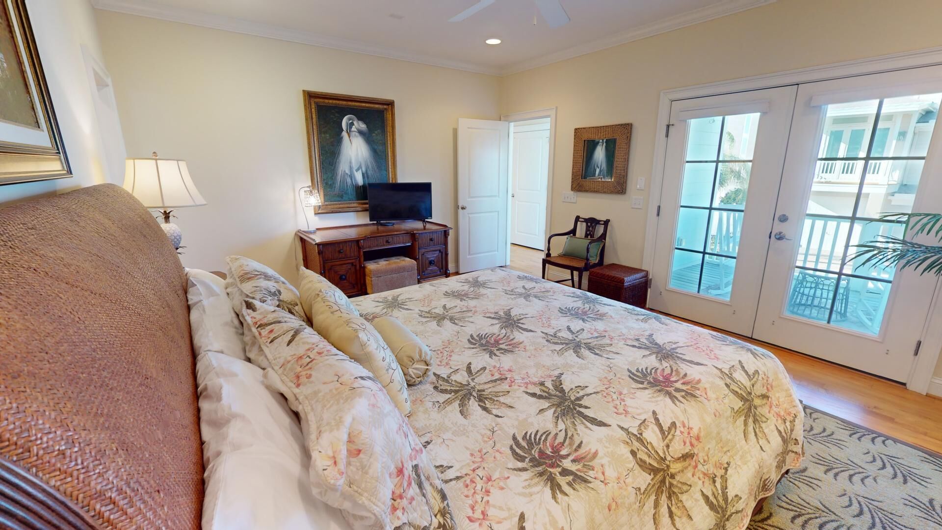 A bedroom with a large bed, a television on a wooden dresser, a door leading to a balcony, and a painting on the wall.