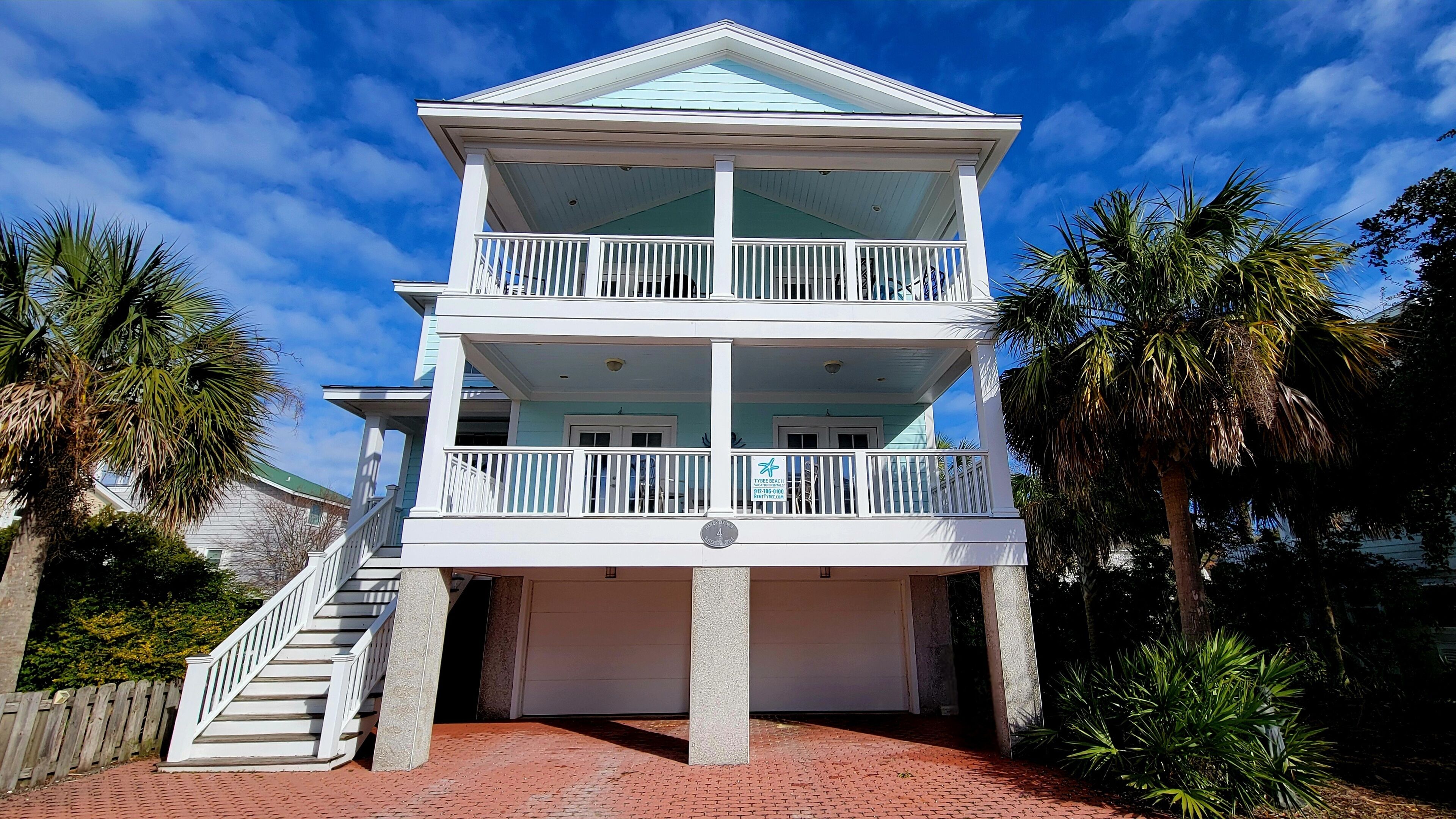 A two-story building with a balcony on each floor, a covered front porch, and a brick pathway leading to the entrance.