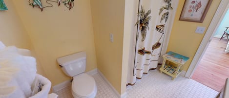 A bathroom with a toilet, a shower curtain with a tropical design, and a small table with a colorful top.