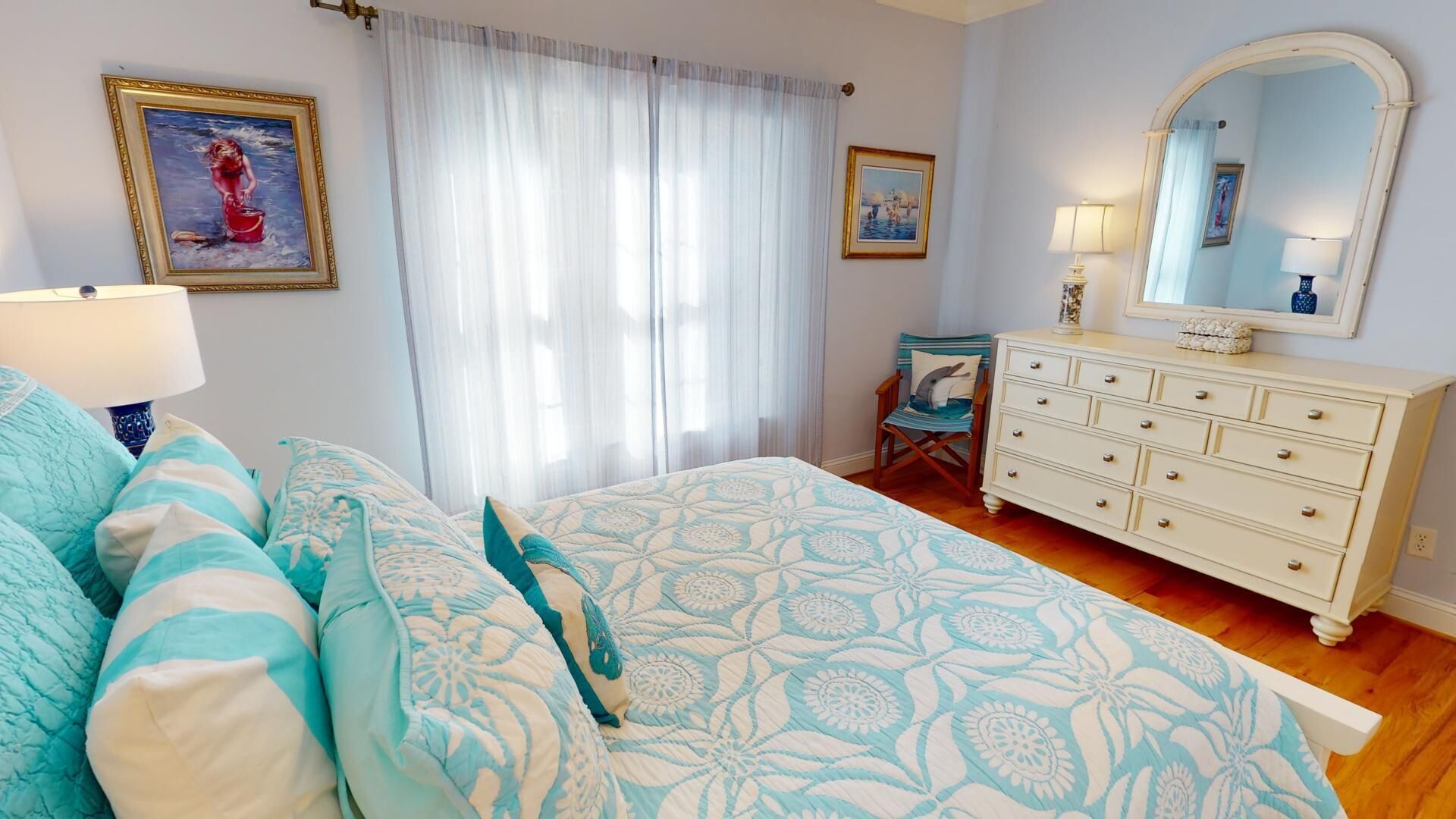 Een slaapkamer met een bed, een kaptafel, een stoel en twee schilderijen aan de muur.