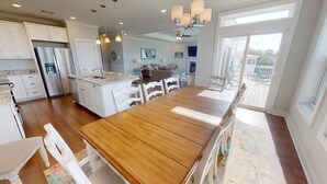 A spacious kitchen with a central island, white cabinetry, and a large dining table. - 50 Captain's View by Tybee Vacation Rentals (Tybee Island)