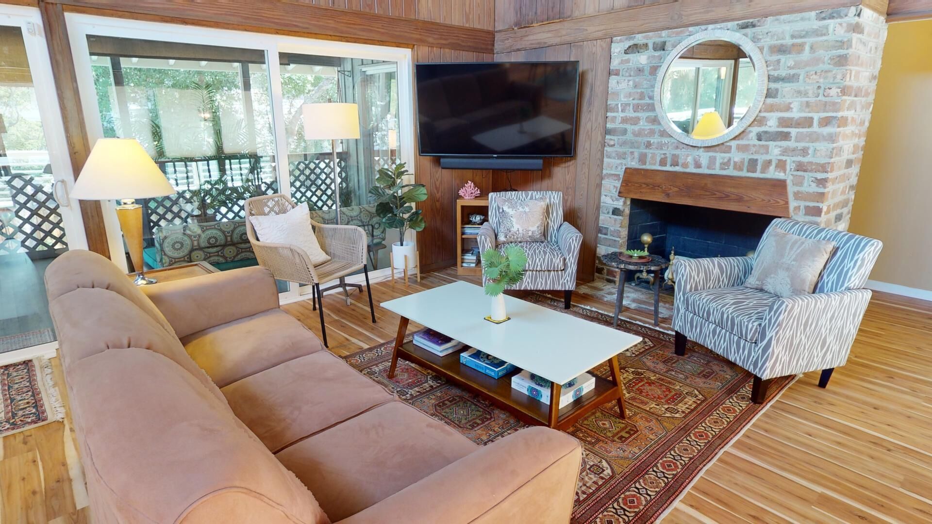 A cozy living room with a sofa, armchairs, a coffee table, and a TV mounted on a brick wall.
