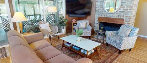 A cozy living room with a sofa, armchairs, a coffee table, and a TV mounted on a brick wall.