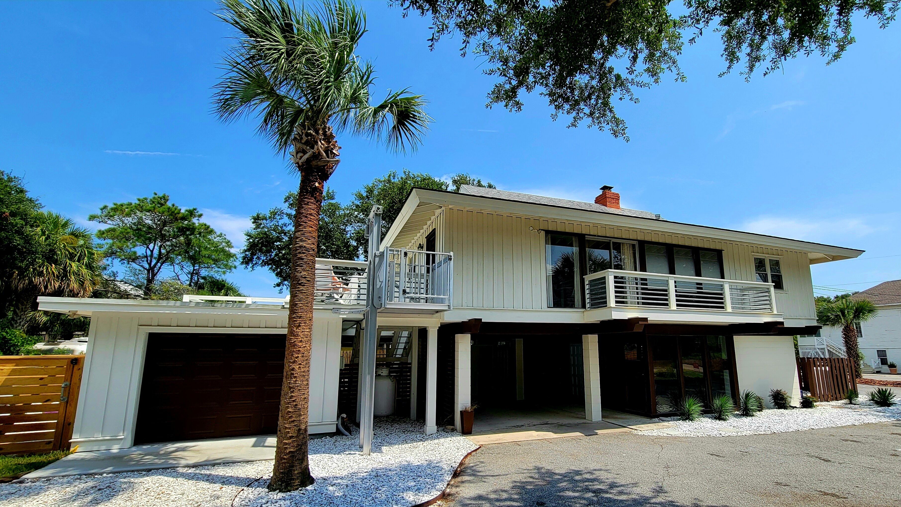 A two-story house with a garage, a balcony, and a palm tree in the front yard.