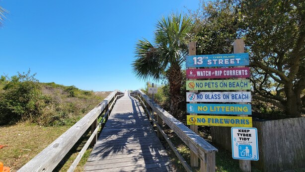 A wooden boardwalk leading to Tybee Island, with signs indicating street name, beach rules, and a reminder to keep the island tidy. - Oceanview Cottage by Tybee Vacation Rentals (Tybee Island)