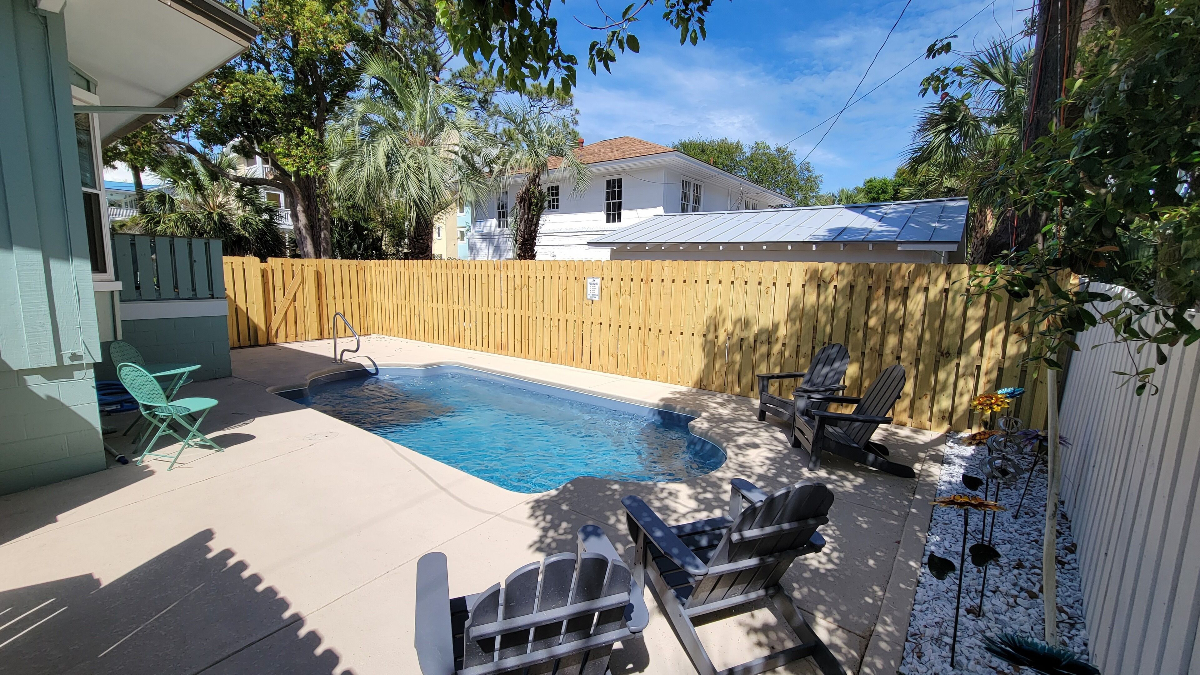 Un jardin avec une piscine, deux fauteuils Adirondack et une clôture en bois.
