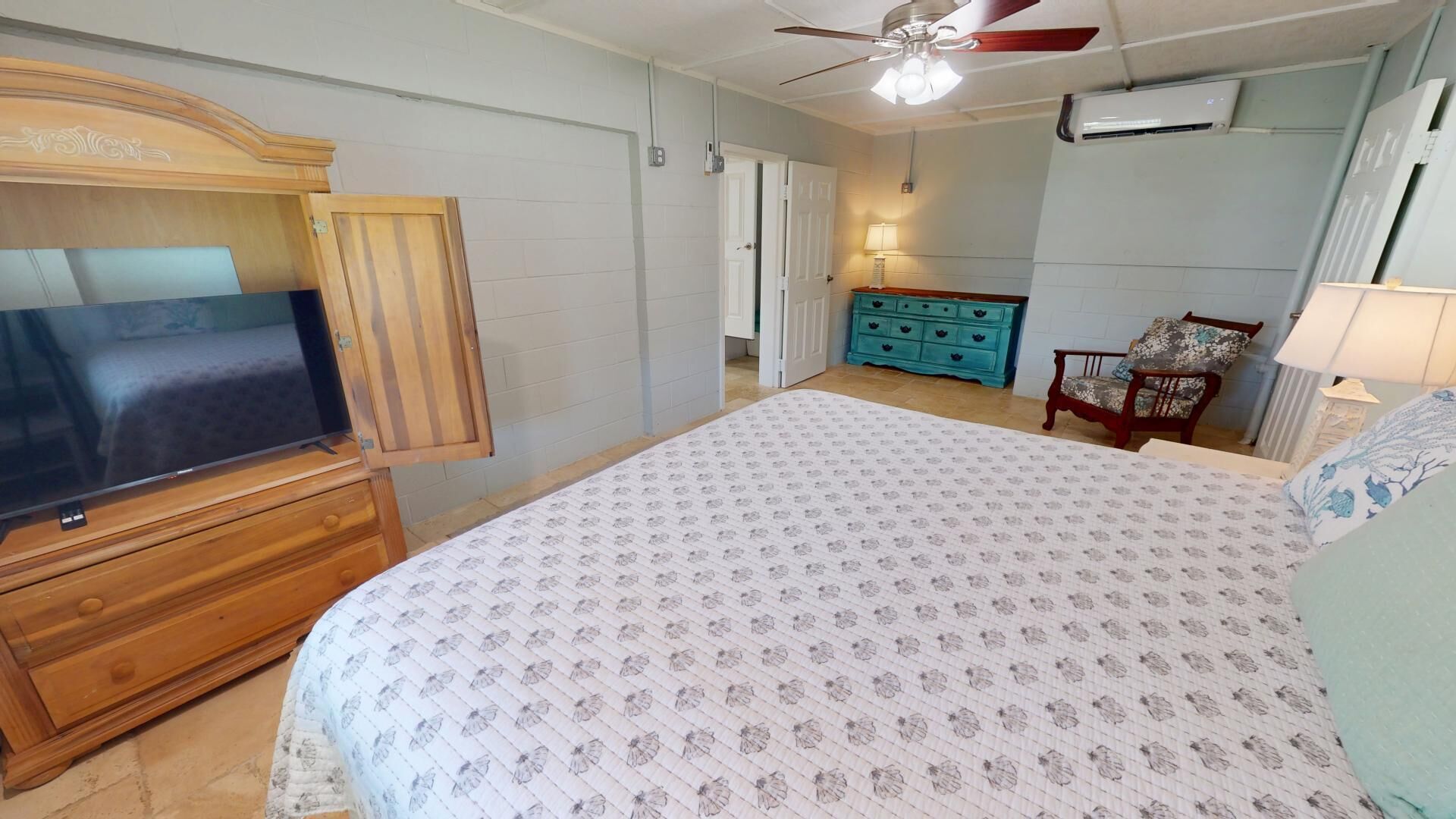 Une chambre à coucher avec un lit, un téléviseur posé sur un meuble en bois, un ventilateur de plafond, une commode et une autre commode bleue.