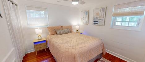 A bedroom with a bed, two bedside tables, a ceiling fan, and two windows with blinds.